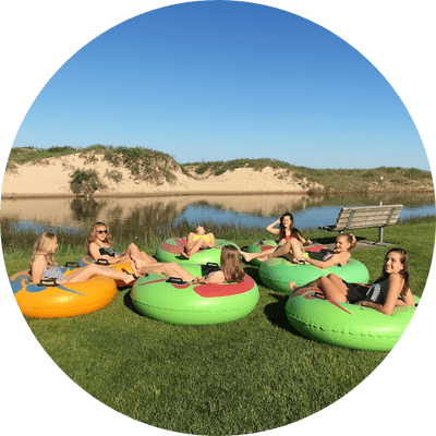 8 group of friends sitting in tubes on grass by the river